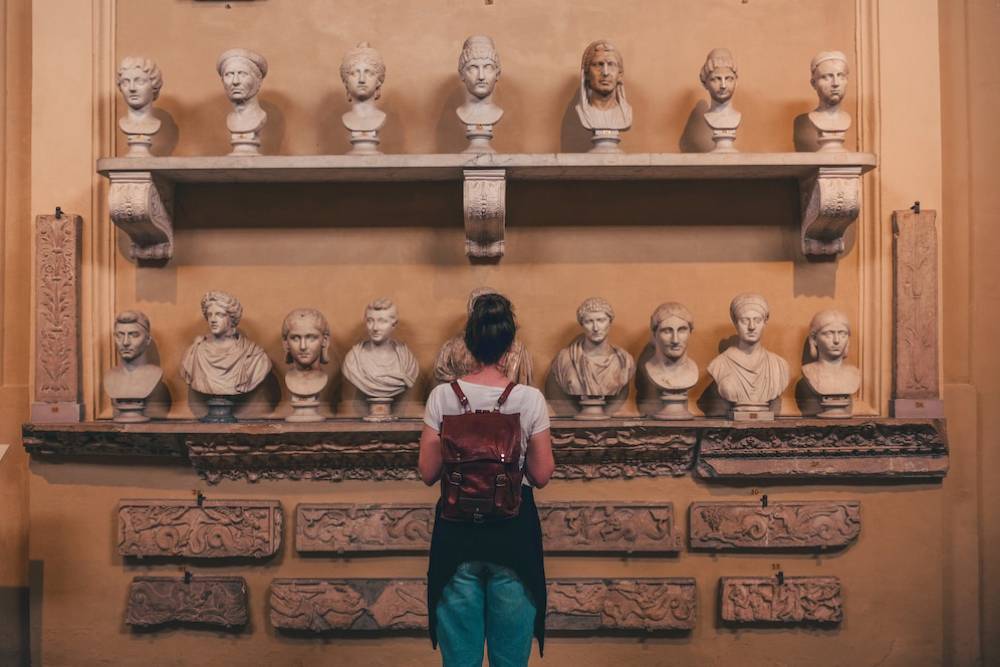A woman observes a collection of ancient busts displayed on shelves in a museum.