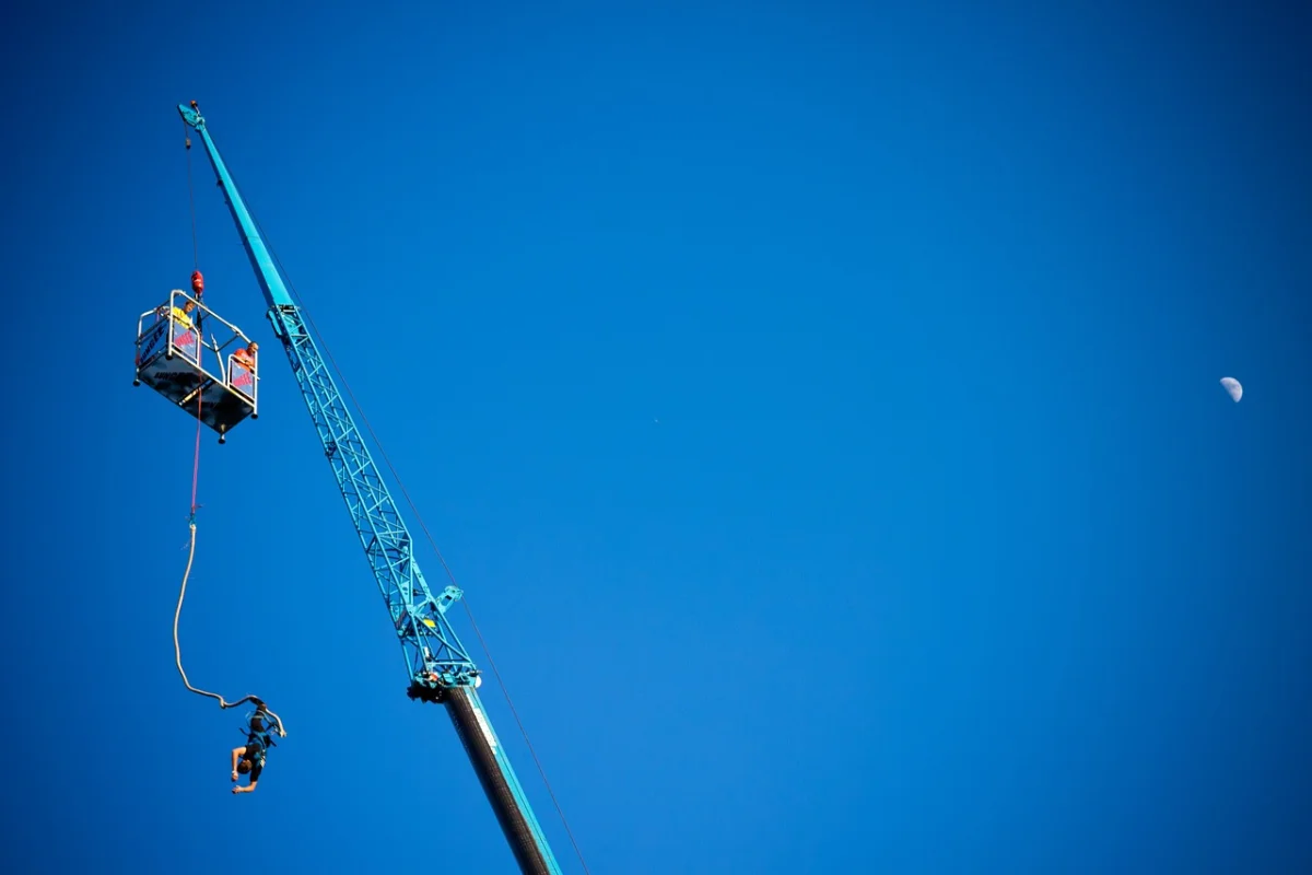 A worker in a high aerial lift against a clear blue sky with a distant moon visible.