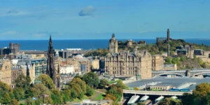 Panoramic view of Edinburgh showing historic buildings and Calton Hill under a clear blue sky.