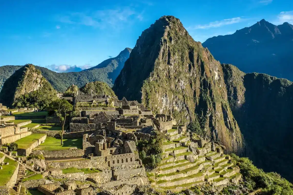 Aerial view of Machu Picchu ruins surrounded by green mountains under a blue sky.