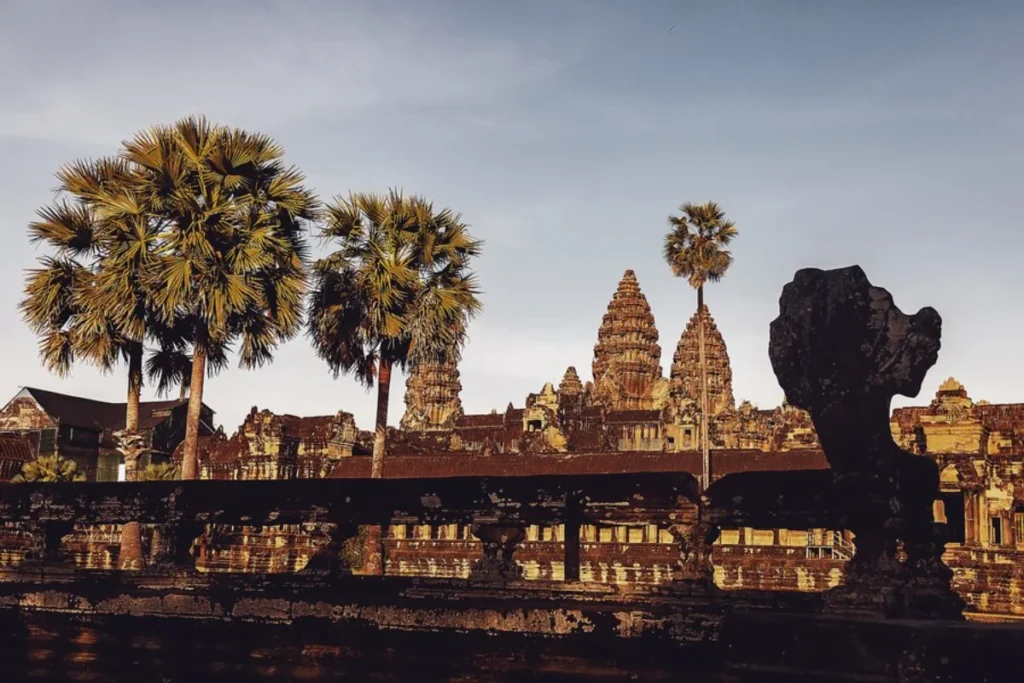 Silhouetted view of ancient Angkor Wat temple with distinctive towers and surrounding palm trees at sunset in Cambodia.