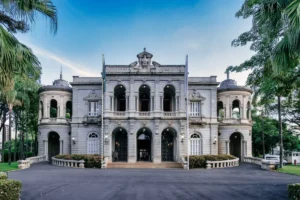 An elegant, historic mansion with classical architecture, surrounded by lush greenery and a clear blue sky.