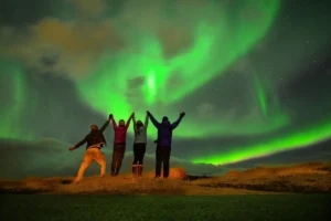 Four people celebrating under the vibrant Northern Lights in a night sky.