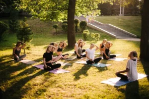 Group of people practicing yoga in a sunny park, with an instructor leading the session.