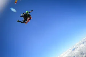 Two skydivers in tandem freefall against a clear blue sky above clouds.