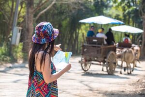 Young girl in a colorful outfit reading a map, with a blurred background featuring people on a horse-drawn cart.