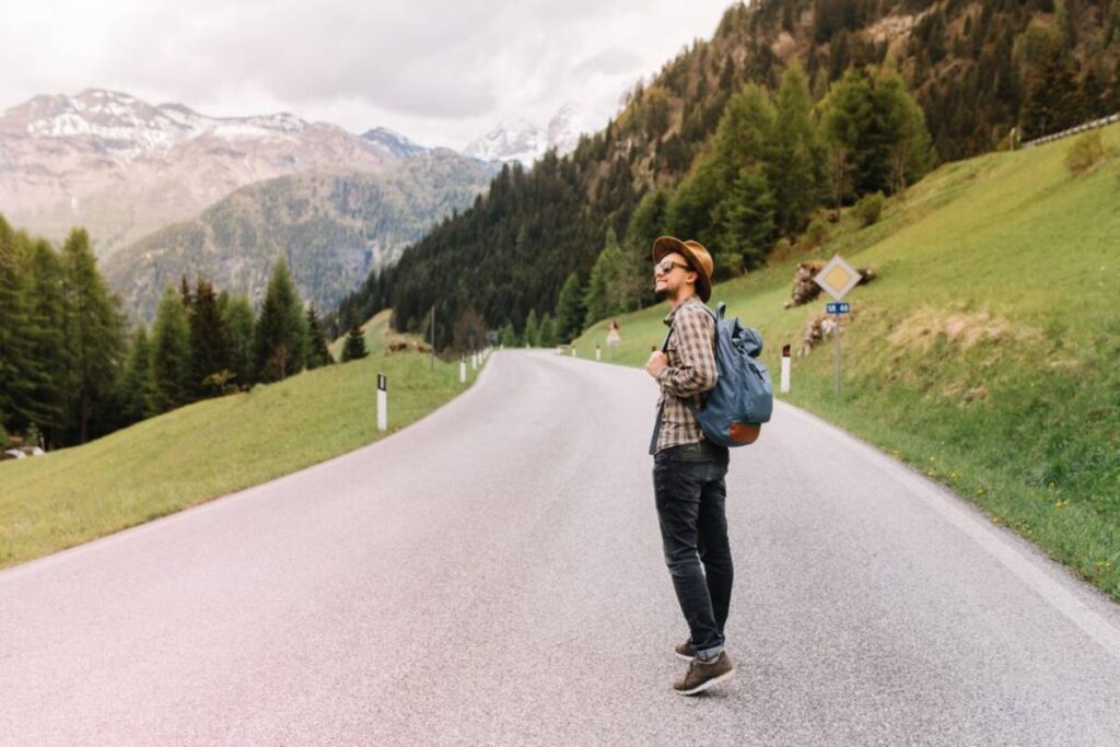 A man with a backpack standing on a mountain road, looking at the scenic landscape.